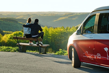 Couple sitting on a Bench in front of a campervan watching the sunset