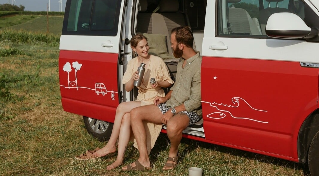 Couple Sitting Outside Of Their Van Drinking From A Reusable Water Bottle