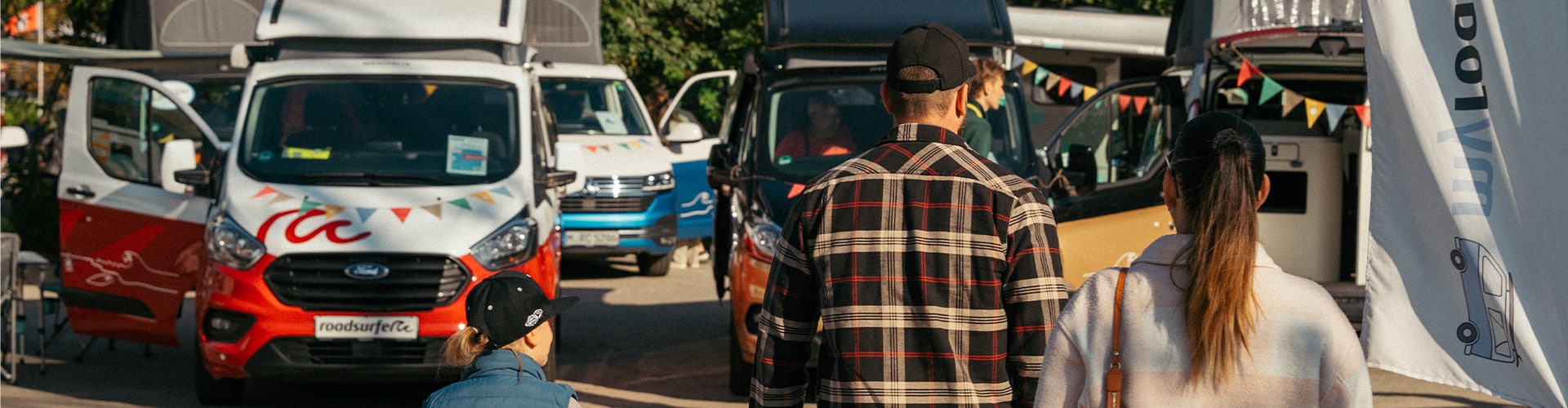Man, woman and child walking towards campervans parked on a sales yard.
