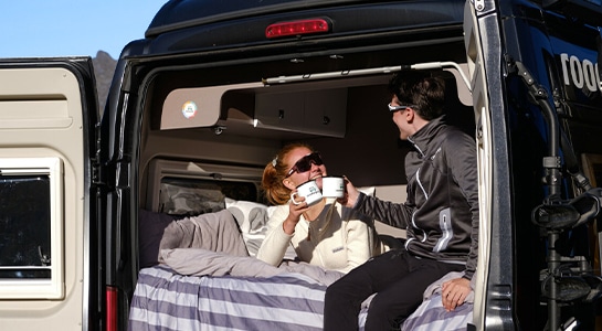couple with sunglasses drinks morning coffee inside a camper van