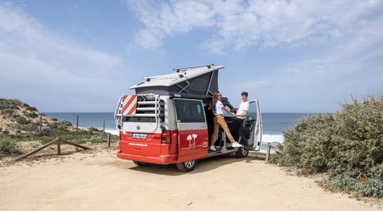 Couple standing on the doorstep of a VW campervan standing at the beach in France