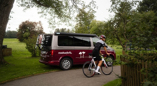 Cyclist sitting on his bike next to a red campervan parked in nature