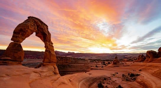 Delicate Arch glowing at sunrise in Arches National Park near Moab, a highlight of many Colorado to California road trip routes.