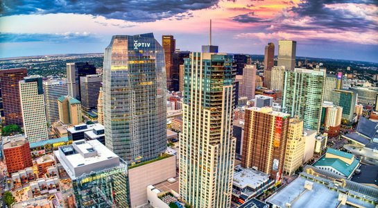 Elevated view of downtown Denver, Colorado, with tall glass buildings glowing under a dramatic pink and blue sunset sky.