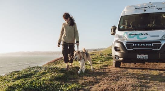 Woman walking her dog on a leash along a coastal bluff next to a roadsurfer camper van