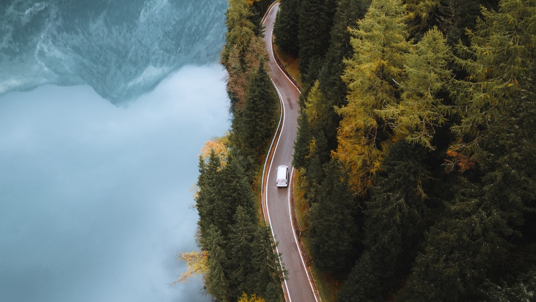 drone shot of a camper van on a scenic road next to a lake