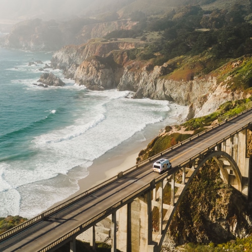 Drone shot of an rv driving over a bridge along a scenic costal road