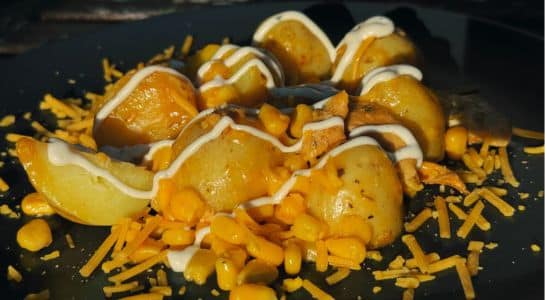 Easy camping recipes roasted potato wedges topped with corn, shredded cheese, and creamy sauce on a dark plate