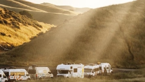 A lineup of RVs parked in golden California hills at sunset, illustrating different rv classes ready for travel.