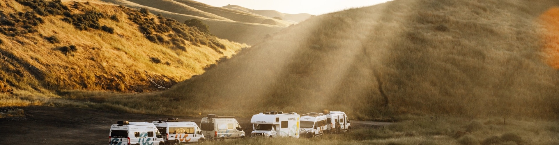 A lineup of RVs parked in golden California hills at sunset, illustrating different rv classes ready for travel.