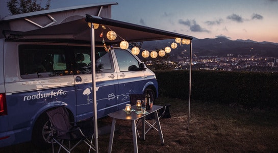 Fairy lights hung around a campervan awning, shining light during the night.