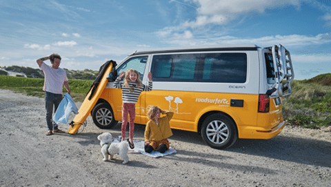 Family with father and two children playing in front of a yellow roadsurfer camper