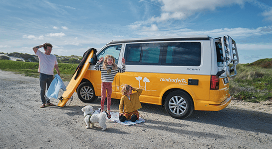 Family with father and two children playing in front of a yellow roadsurfer camper