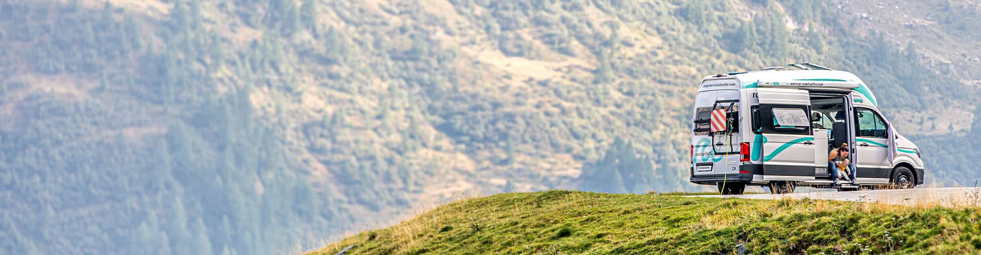 Family Finca RV sprinter van camper from roadsurfer in the mountains, woman playing with baby sitting in the doorway