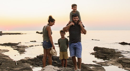 Family of four on a pebble beach during sunset.