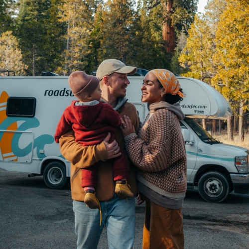 Family of three standing and cuddling in front of a roadsurfer rv