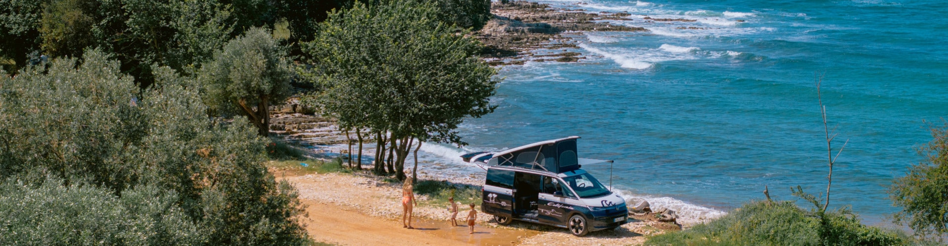 Mother and her two sons playing in front of the campervan parked at the beachfront.
