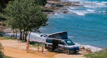 Mother and her two sons playing in front of the campervan parked at the beachfront.