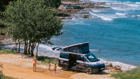 Mother and her two sons playing in front of the campervan parked at the beachfront.