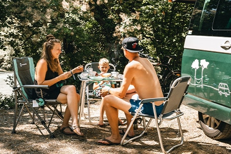 Family with kid sitting next to campervan