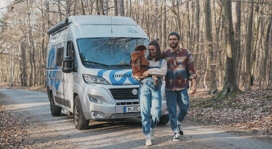 Family with child walking through a forest and a Fiat Ducato campervan standing behind.