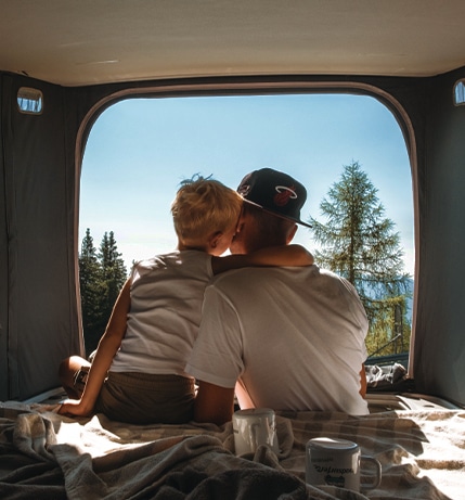 Father and Son cuddling in the back of a campervan enjoying the view