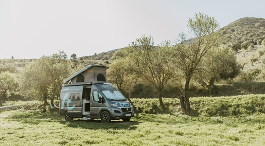 A grey Fiat Ducato campervan from roadsurfer standing with open roof on a field in the middle of the mountains in Spain