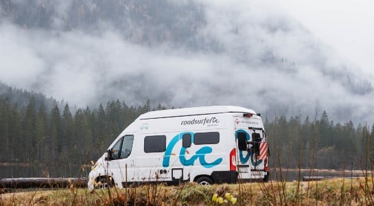 A Fiat Ducato Boxvan with a cloudy landscape of trees and mountains in the back