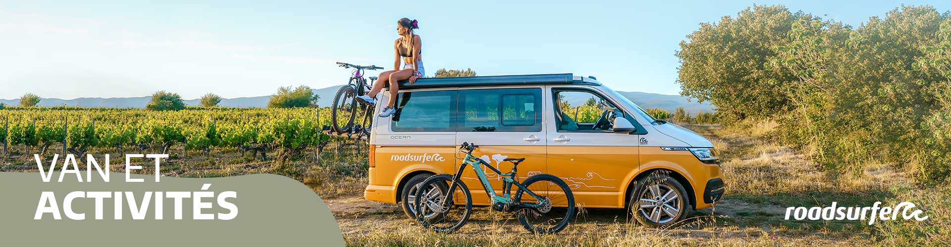 Fille assise sur le toit d'un van aménagé au mileu des vignes avec porte-vélos