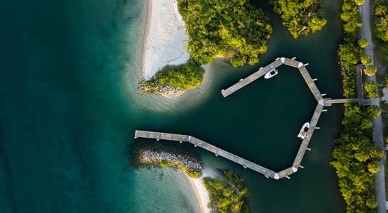 Aerial view of a small marina along Florida’s coast, with turquoise water, sandy shores, and lush green mangroves surrounding a winding dock
