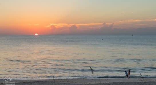 Peaceful sunrise on a Florida beach with a couple walking along the shoreline as the sun rises over the horizon.