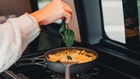 Hand adding basil to pot of food in a camper.