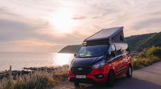 Red Ford Nugget Camper standing near to a cliff with sundown in the background