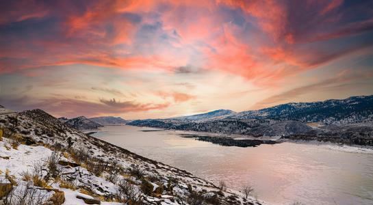 Sunrise over Horsetooth Reservoir near Fort Collins, Colorado, with snow-covered hills and vibrant pink clouds reflected on the water.