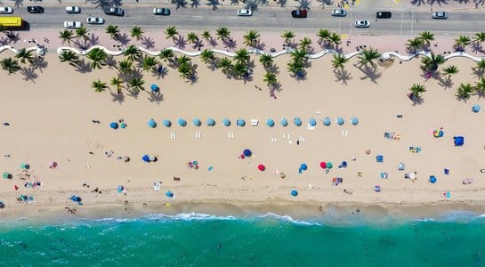 Aerial view of Fort Lauderdale Beach, Florida, with umbrellas, palm trees, and turquoise ocean water