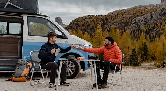 friends at a camping table drinking coffee in an autumn landscape
