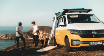 three friends with surfboards and a yellow campervan at the ocean