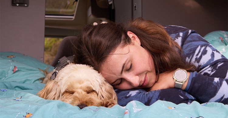 Girl cuddling a sleeping dog on the bed of a boxvan.