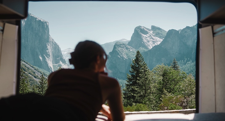 Girl enjoying a scenic view on mountains and forest from the back of a campervan