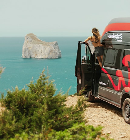 Girl looking out of a camper door at a cliff watching the blue ocean