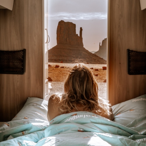 Girl lying in bed looking outside the back of rv facing a scenic rock formation