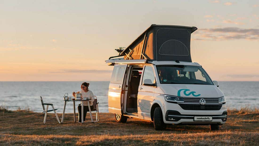 Girl sitting in front of a campervan having dinner at sunset