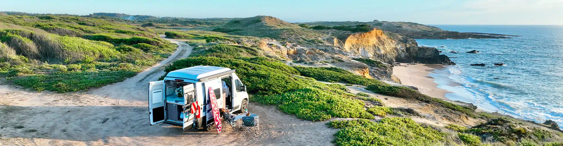 Girl Sitting In Front Of A Campervan Parked In Front Of The Sea