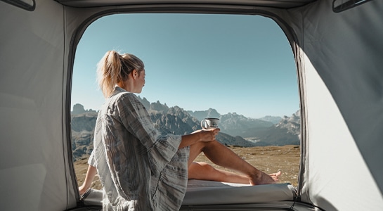 girl sitting in the pop up tent of a camper van with a coffee