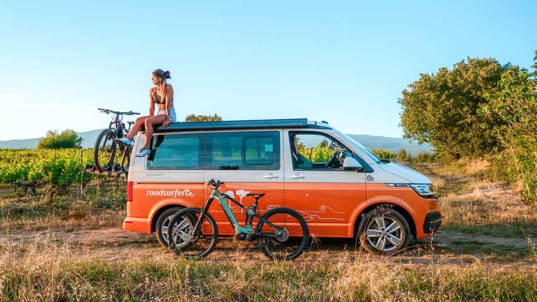 girl sitting on the roof of a campervan ready for mountainbiking