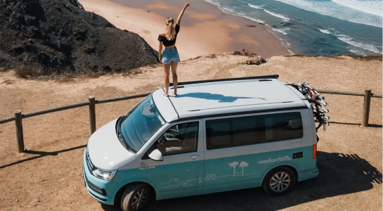 girl standing on a campervan next to the ocean