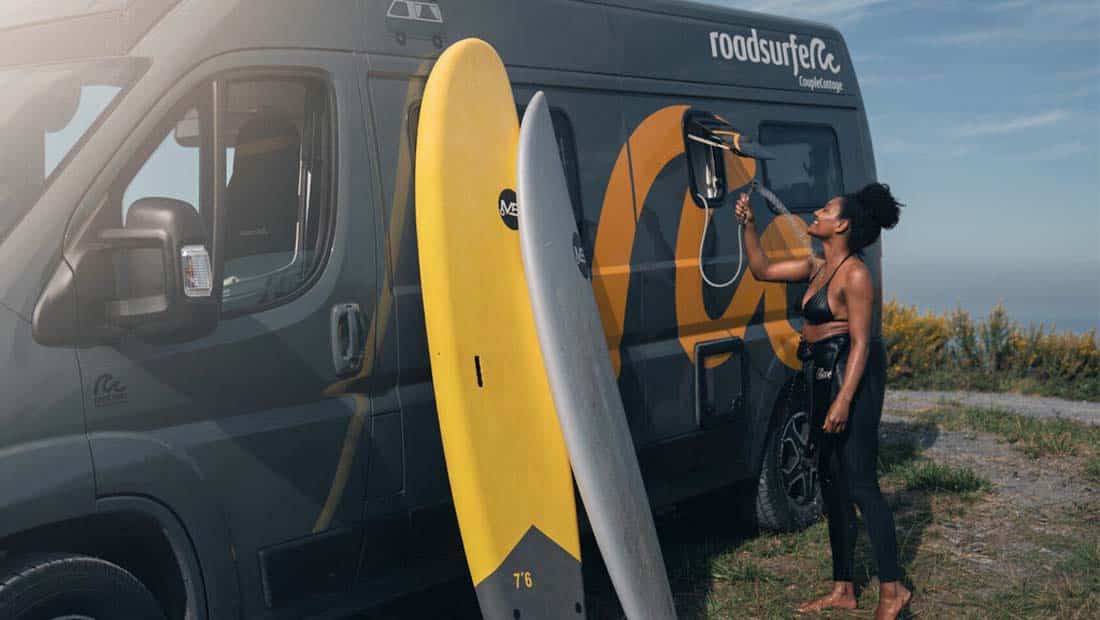 Girl taking a shower at the outdoor shower of a campervan after surfing