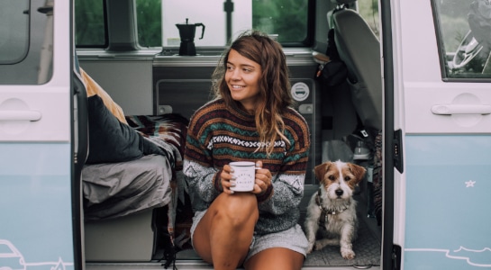 Girl with cute little dog sitting in a cozy campervan with a cup of coffee