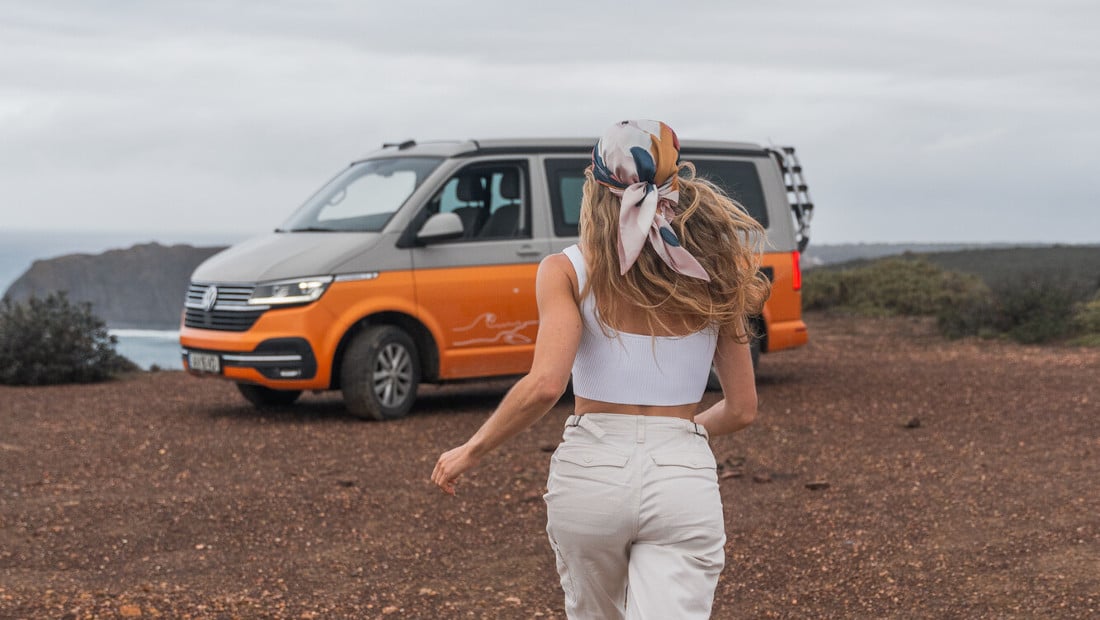 girl with long hair running towards a camper van