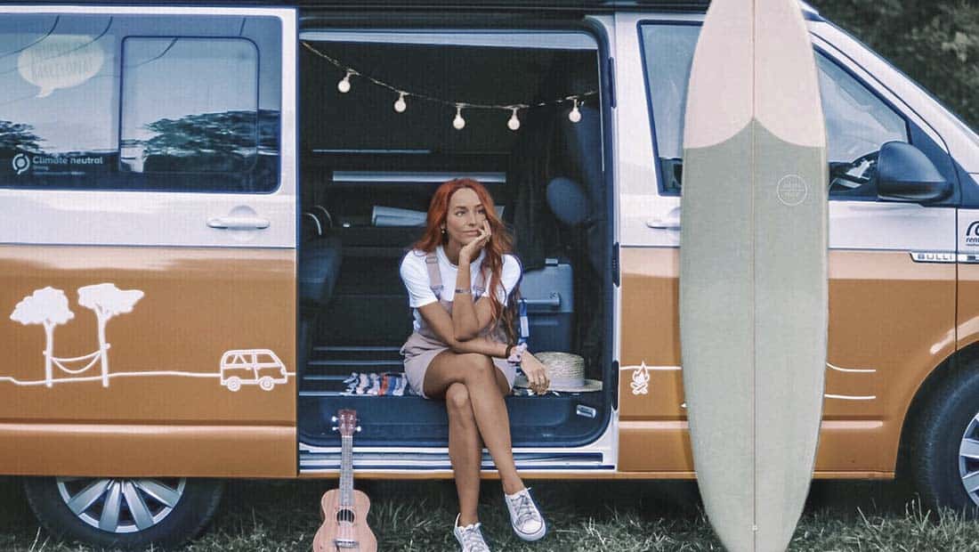girl with surfboard and ukulele sitting in a campervan